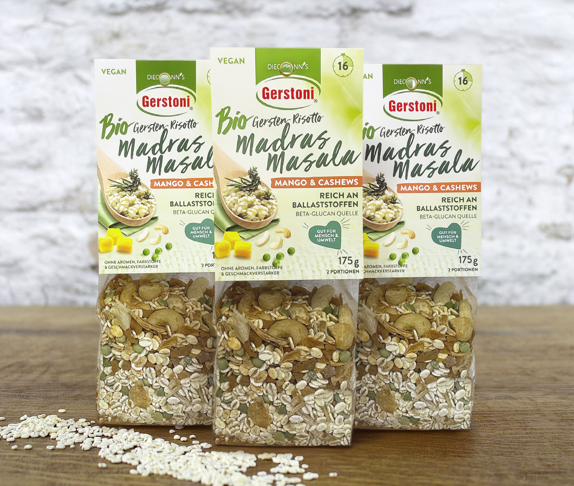 3 Packungen BIO Gersten-Risotto Madras Masala auf Holztisch stehend vor weißer Backsteinmauer