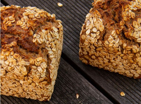 Zwei Brotlaibe Dinkelvollkornbrot mit Gerstoni Gourmet Gerste  liegend auf dunklem Holztisch