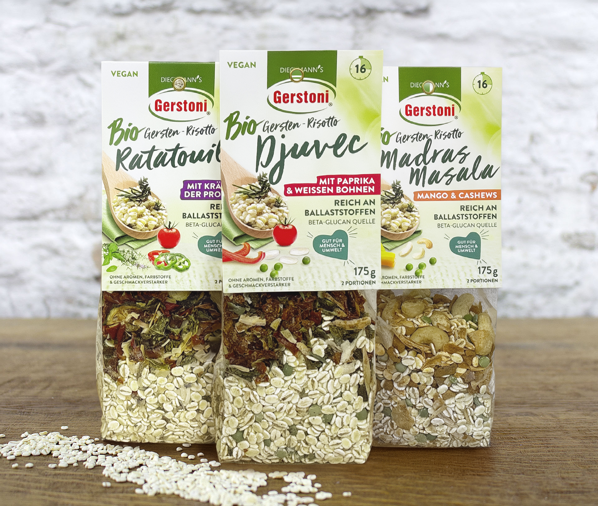 3 Pack Bio Gerstoni Gersten-Risottos auf Holztisch vor einer weißen Backsteinmauer