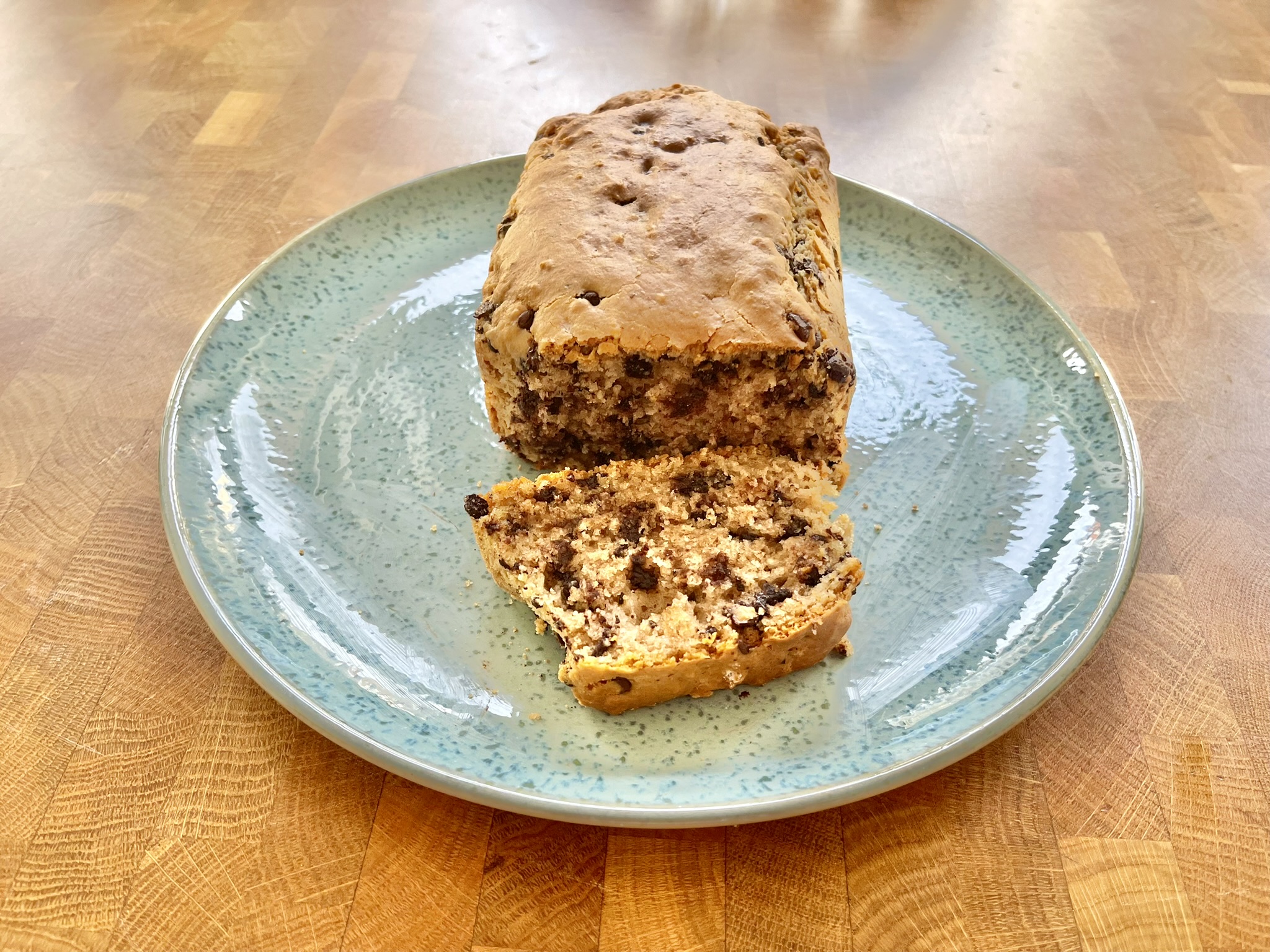 Ein angeschnittener Rührkuchen mit Schokostückchen auf einem blauen Teller.